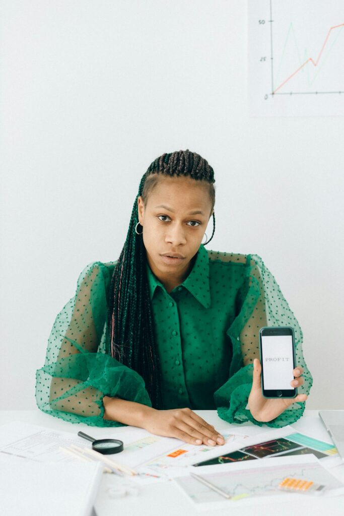 Businesswoman sitting at a desk analyzing charts with a smartphone, highlighting finance and technology.